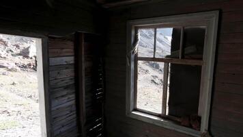 visie door de ramen binnen een houten verlaten huis. klem. oud geruïneerd houten gebouw en een heuvel helling buiten. video