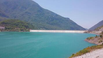 Top view of blue reservoir in mountains. Clip. Behind the trees is beautiful landscape with turquoise lake and green mountains on clear day. Turquoise reservoir in mountains in south video