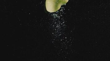 Close up of an apple half thrown in the water isolated on black background. Action. Green apple in transparent water with bubbles of air, concept of vitamins and healthy diet. video