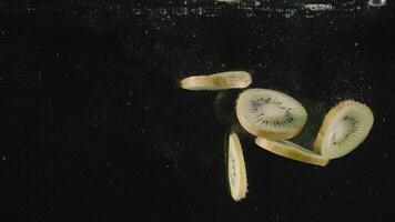 Scheiben von Kiwi Obst fallen in Wasser voll von Luftblasen im schleppend Bewegung. Aktion. schließen oben von Schnitt tropisch Obst fallen unter Wasser isoliert auf schwarz Hintergrund. video