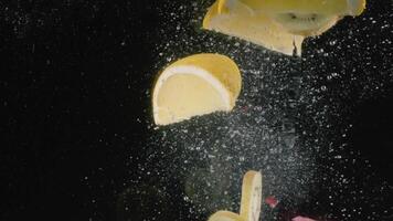 Close up of lemon, kiwi slices, grapes and half of pomegranate thrown in the water isolated on black background. Action. Fruits and berries in transparent water with bubbles of air, concept of video