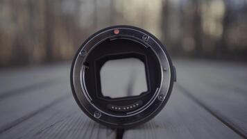 Close up of professional camera lens with opened aperture. Action. Technical features of lens for professional camera, camera lens lying on a wooden bench in a city park. video