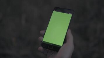 fechar acima do uma homem mão segurando Smartphone com verde tela. estoque. moderno Móvel telefone com croma chave em borrado fundo. video