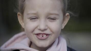 cerca arriba de el linda cara de un pequeño niña bizco debajo el luz de sol. acción. el niño es sonriente y diciendo alguna cosa mientras su pelo halagador en el viento. video