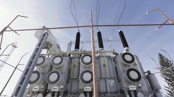 High voltage electrical substation on blue cloudy sky background. Action. Bottom view of a transformer near street lamps, concept of energy system. video