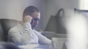 zakenman werken in zijn kantoor in voorkant van computer scherm. actie. kant visie van mannetje in een overhemd pratend Aan zijn mobiel telefoon over werk. video