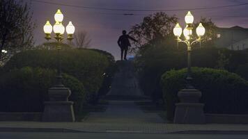 arrière vue de une monument dans le Nom de Jacob Sverdlov dans Ekaterinbourg, Russie. Stock images. en retard soir dans le rue avec vert ruelle et rue lanternes de premier plan à le sculpture. video