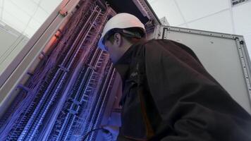 electricista trabajando con alambrado en eléctrico caja, fijación conexiones acción. fondo ver de un electricista en un protector uniforme y casco a el poder planta. video