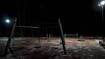 Night view of children playground and lanterns. Action. Empty winter playground with swings and sports equipment on black sky background. video