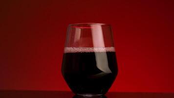 ciliegia o Melograno succo è versato in un' bicchiere. azione filmato. vicino su di scrosciante rosso succo in trasparente bicchiere isolato su rosso sfondo. video