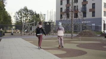 posteriore Visualizza di un' ragazzo su un' scooter e un' ragazza a piedi su bambini terreno di gioco vicino alto salire Residenziale costruzione. azione. concetto di contento infanzia. video