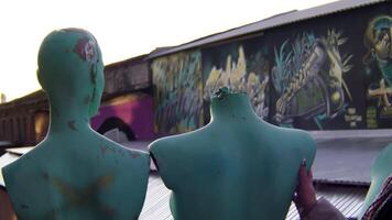 azul manequins em pé em a fundo do a velho construção coberto de grafite. estoque imagens de vídeo. moderno arte objeto e uma mulher com colorida afro tranças. video