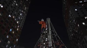 Happy little girl playing outdoors late in the evening. Action. Bottom view of a smiling girl on the top of net pyramid waving to the camera on black sky and high rise residential buildings background video