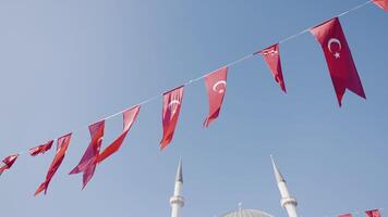 kalkoen, Istanbul-december, 2020. Turks vlaggen Aan blauw lucht achtergrond. actie. feestelijk lint met Turks vlaggen fladderend in wind. Turks vlaggen hangen Aan feestelijk touw Aan achtergrond van minaretten video