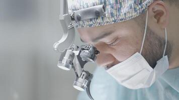 Close-up of surgeon performing operation. Action. Attentive and focused gaze of surgeon during operation. Professional surgeon with binoculars performs operation video