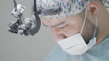 Close-up of surgeon performing operation. Action. Attentive and focused gaze of surgeon during operation. Professional surgeon with binoculars performs operation video