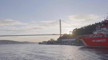 Turkey, Istanbul-December, 2020. Ship off coast of sea city. Action. Steamboat sails near shore of Istanbul on background of suspension bridge on sunny day. Ships and steamers sailing off coast of video