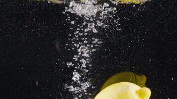 Close-up of whole lemon falling into water. Action. Whole lemon falls into water with bubbles on black background. Refreshing lemon drops into water video