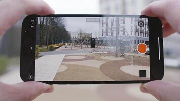 närbild av skärm av telefon tar video. handling. man innehar telefon och tar video av lekplats och flera våningar byggnad