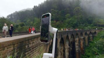 tiroteio em tripé telefone enquanto viajando. Ação. tiroteio vídeo em telefone com estabilizador enquanto viajando. tiroteio ponte com estrada de ferro dentro selva em telefone para blog video