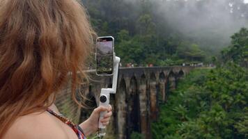 donna prende su Telefono con pietra ponte e verde montagne. azione. bellissimo donna spara blog nel tropicale montagne. donna prende bellissimo visualizzazioni di giungla e pietra ponte su Telefono video