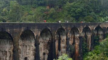Touristen gehen auf Stein Brücke im Dschungel. Aktion. Menschen gehen auf uralt Stein Brücke im Regenwald. schön Landschaft mit Menschen auf Aquädukt und Grün Hügel video