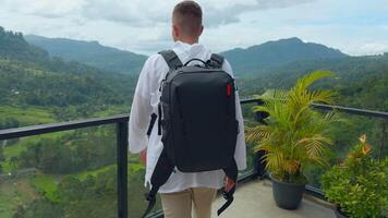 Man with view of tropical mountain valley. Action. Man on observation deck in tropical mountains. Man with backpack on sightseeing attraction overlooking green mountains video