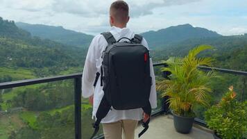 Man with view of tropical mountain valley. Action. Man on observation deck in tropical mountains. Man with backpack on sightseeing attraction overlooking green mountains video