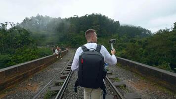 kaukasisch Reisender Mann Aufzeichnung Video von Grün Berg Landschaft. Aktion. Mann Gehen auf Eisenbahn mit Rucksack.