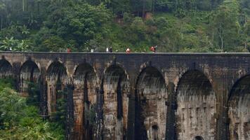 turistas andar em pedra ponte dentro selva. Ação. pessoas andar em antigo pedra ponte dentro floresta tropical. lindo panorama com pessoas em aqueduto e verde colinas video