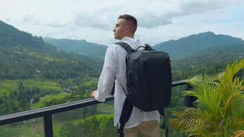 Man with view of tropical mountain valley. Action. Man on observation deck in tropical mountains. Man with backpack on sightseeing attraction overlooking green mountains video