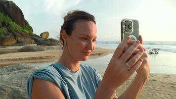 mooi jong Kaukasisch vrouw duurt afbeeldingen van de mooi zee Aan tropisch eiland strand. actie. gelukkig meisje Aan vakantie foto's Aan smartphone met palm bomen Aan de achtergrond. video