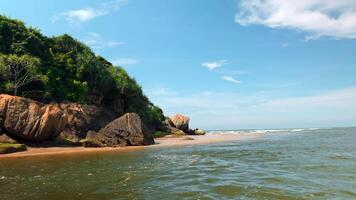 Beautiful view from sea to shore with rocks and tropical trees on sunny day. Action. Boat trip along tropical coast with rocks. Beautiful water on coast with rocks and tropical vegetation video