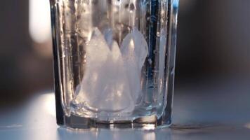 Wet empty transparent glass with ice pieces. Concept. Close up of putting ice pieces into the faceted glass standing on white table on blurred background. video