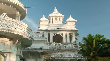 White Indian Temple with palm tree. Action. Beautiful white temple with Buddhist patterns. White Buddhist temple with palm trees on sunny summer day video