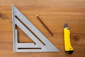 Swanson's aluminum roofing square, pencil and knife on a wooden table photo