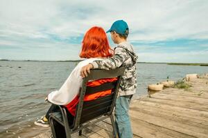 Generacion z niña con rojo pelo y hermano abrazando por tranquilo lago foto