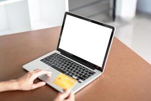 Woman shopping online using laptop holding a credit card at the home. Mock up laptop photo