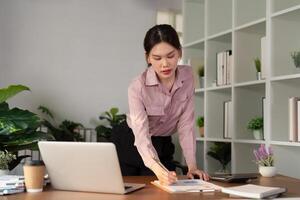 Asian Businesswoman using laptop computer and working at home with calculator document on desk, doing planning analyzing the financial report, business plan investment, finance analysis concept photo