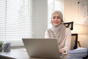 asiático musulmán mujer de negocios en hijab cabeza bufanda trabajando con papel documento en el moderno oficina. diversidad y oficina concepto foto