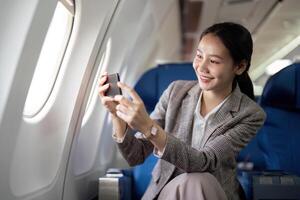 Asian young businesswoman successful or female entrepreneur in formal suit in a plane sit in a business class seat and uses a smartphone during flight. Traveling and Business concept photo