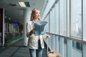 contento joven mujer asiático es estar en aeropuerto cerca maleta y leyendo mapa foto