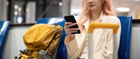 turista mujer utilizando móvil teléfono inteligente con maleta de viaje Entre murga para vuelo en aeropuerto Terminal, vuelo cheque en, turista viaje viaje concepto foto