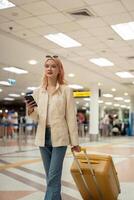 un mujer asiático caminando en un aeropuerto. móvil, maleta y viaje con un joven hembra en un internacional viaje para trabajo o viaje foto