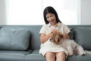 mayor asiático mujer contento y un perro en el Mañana a hogar interior, soltero mayor retirado hembra sentado en sofá en vivo habitación foto