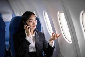 Asian young businesswoman successful or female entrepreneur in formal suit in a plane sit in a business class seat and uses a smartphone during flight. Traveling and Business concept photo