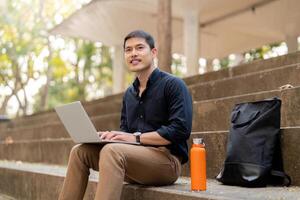 Asian businessman with reusable eco friendly ecological cup using laptop and sitting outside the office building. Eco friendly, sustainable lifestyle concept photo