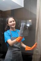 asiático mujer limpieza el vaso en el departamento. limpieza personal mantener limpieza en con toalla y rociar detergente foto