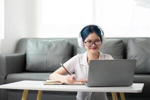 Happy young woman teenage wearing headphones writing note. student online learning class study online video call zoom teacher with laptop and book photo