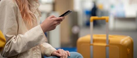 turista mujer utilizando móvil teléfono inteligente con maleta de viaje Entre murga para vuelo en aeropuerto Terminal, vuelo cheque en, turista viaje viaje concepto foto